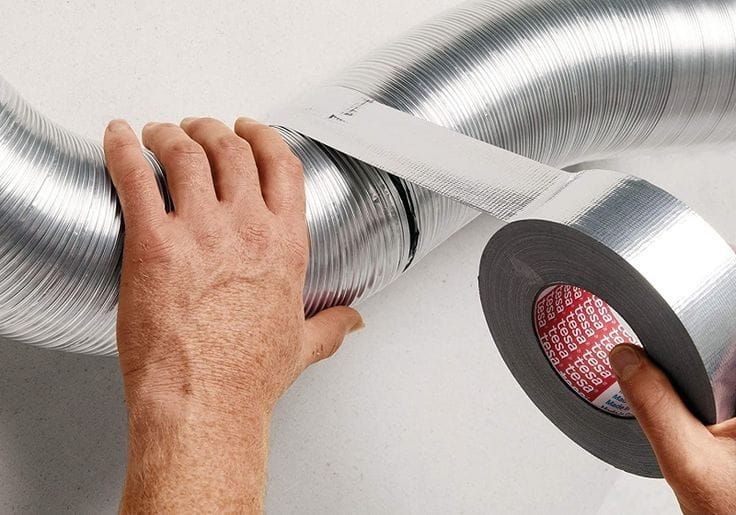 Technician applying aluminium foil tape to seal an HVAC air duct for insulation and airtight ventilation in Kenya.